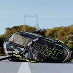 Raqueteira Babolat RH6 Pure Aero preta e amarela, vista de perto com uma raquete de tênis Babolat por cima, em uma quadra de tênis externa.