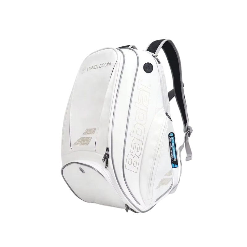 A imagem mostra uma mochila raqueteira da marca Babolat, de cor branca, com detalhes em prata e preto. A mochila tem o logo da Babolat em destaque na parte frontal, com um design moderno e minimalista. Ela apresenta um compartimento principal grande e um bolso lateral para fácil acesso, ideal para carregar raquetes de tênis ou beach tennis com segurança. As alças acolchoadas garantem conforto ao carregar a mochila. A mochila também apresenta a inscrição "Wimbledon", reforçando sua conexão com o famoso torne
