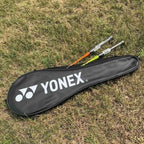 Raqueteira Yonex preta deitada na grama com duas raquetes de badminton parcialmente para fora da capa.