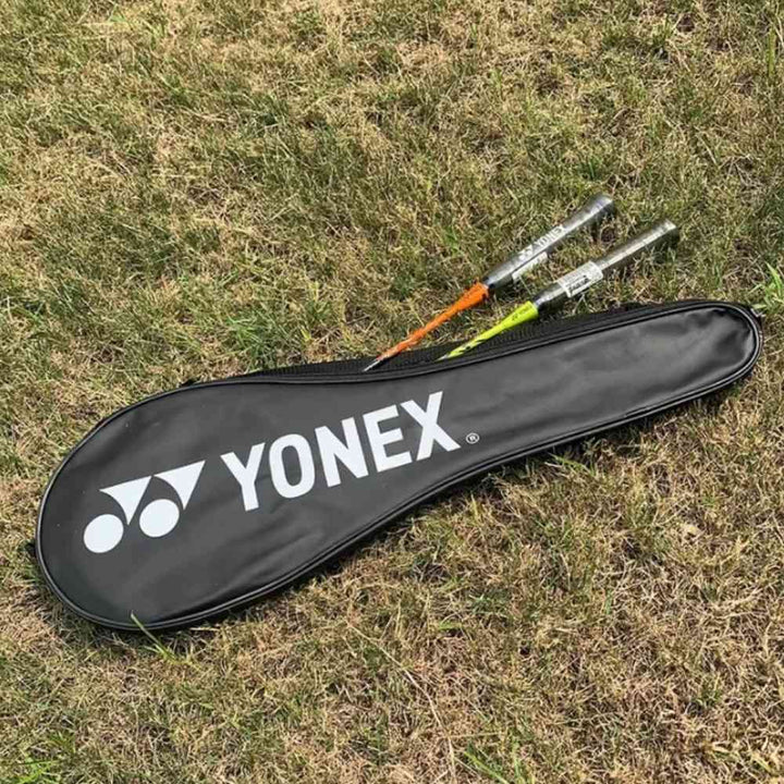 Raqueteira Yonex preta deitada na grama com duas raquetes de badminton parcialmente para fora da capa.