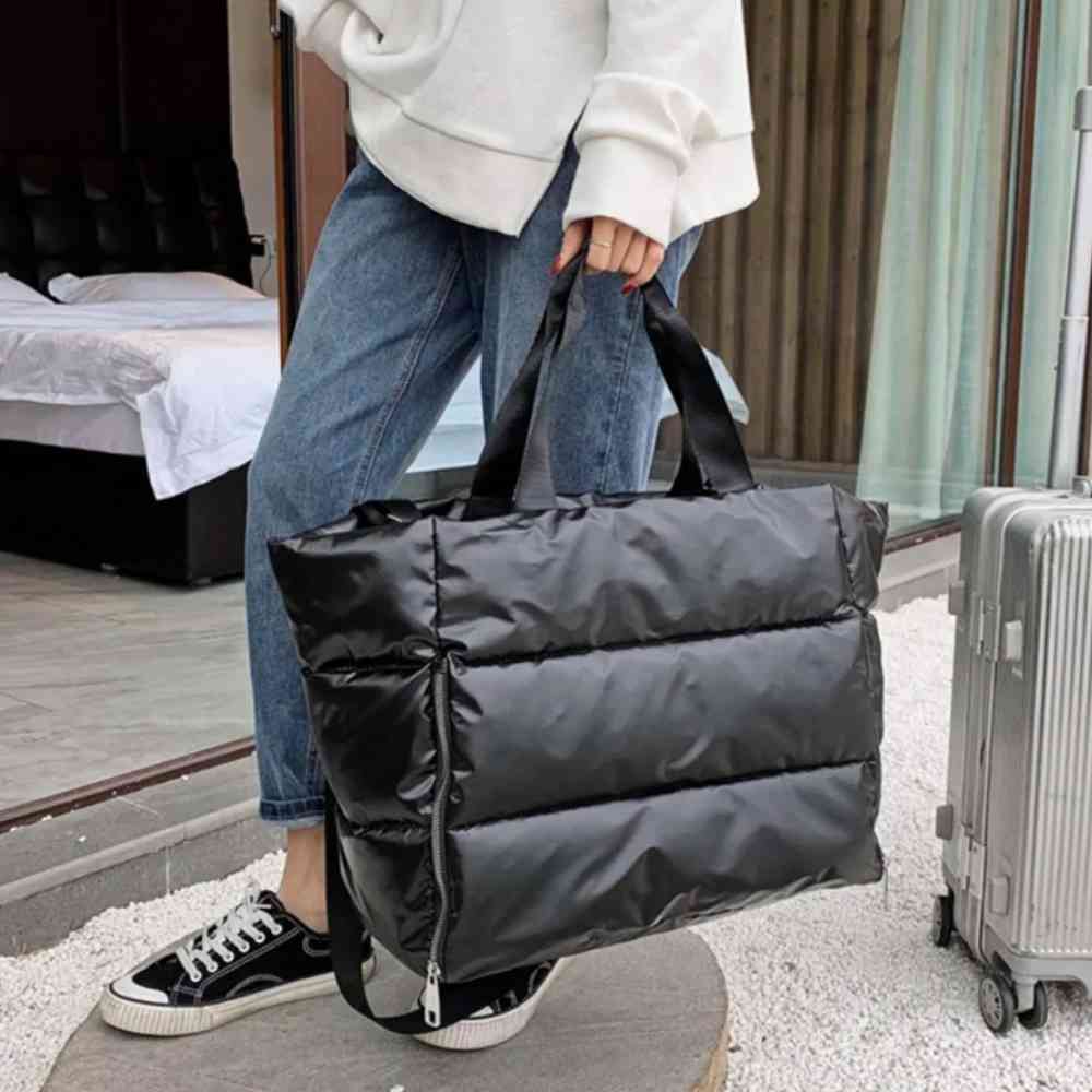 Pessoa carregando a Bolsa de Academia Feminina Grande para Yoga com Compartimento para Mat Preta Urbanno pela alça de mão, ao lado de uma mala de viagem, demonstrando sua praticidade para viagens ou transporte.