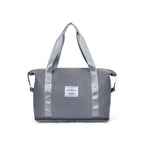 Bolsa de Academia e Viagem Feminina Leve Expansível Cinza Urbanno, vista frontal em seu estado compacto, com alças duplas e etiqueta da marca, pronta para ser expandida e usada.