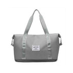 Bolsa de Academia e Viagem Feminina Leve Expansível Cinza Urbanno, vista frontal, com design espaçoso e etiqueta da marca na frente, ideal para praticidade no dia a dia e viagens.