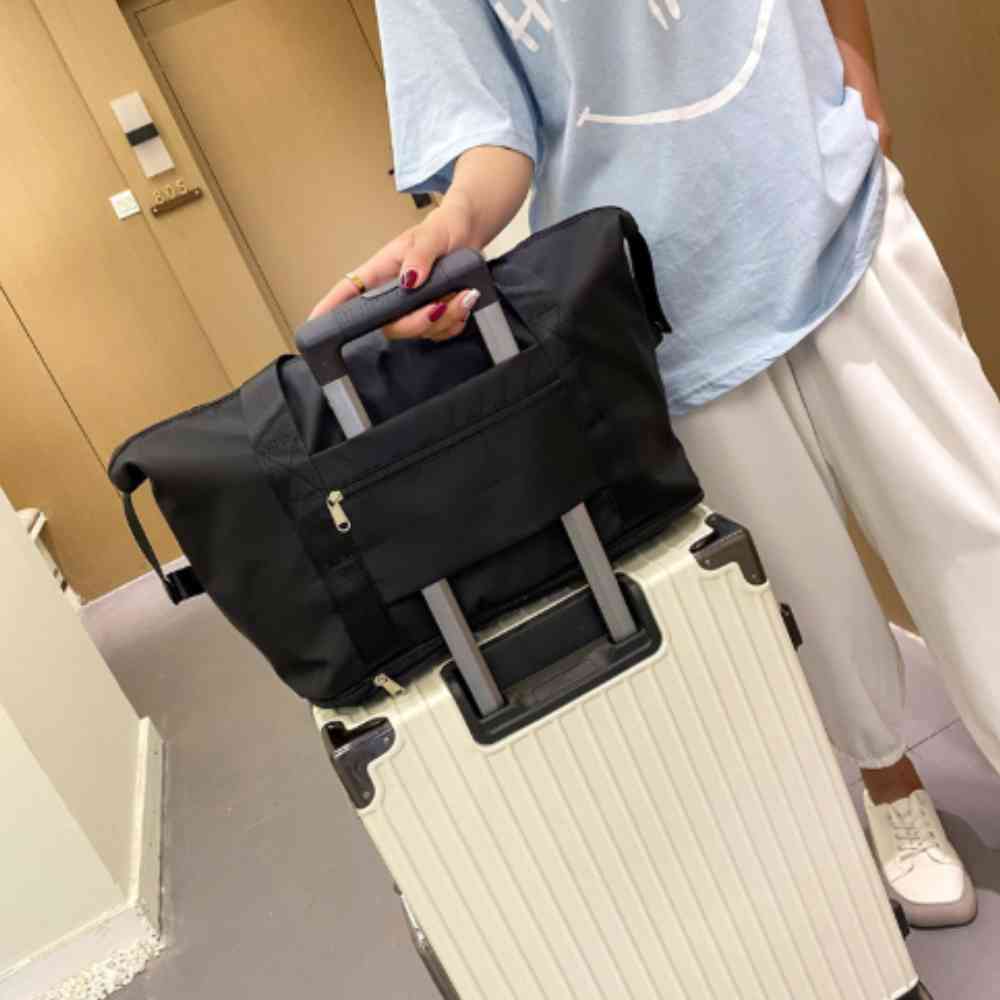 Bolsa de Academia e Viagem Feminina Leve Expansível Preta Urbanno, acoplada à alça retrátil de uma mala de viagem clara, sendo transportada por uma pessoa, demonstrando sua praticidade para viagens.