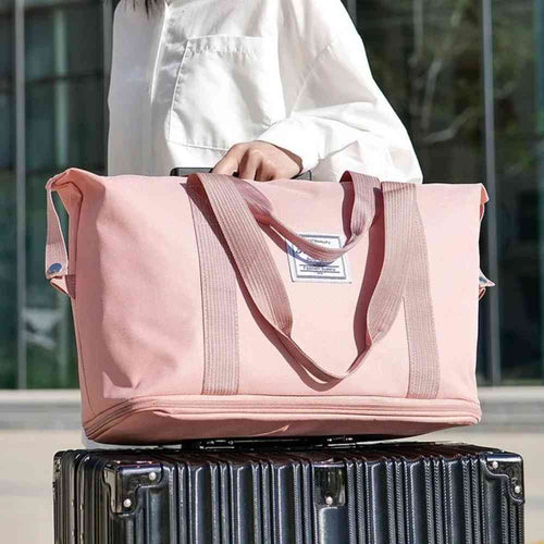 Bolsa de Academia e Viagem Feminina Leve Expansível Rosa Urbanno, acoplada à alça retrátil de uma mala de viagem escura, sendo transportada por uma pessoa, demonstrando sua praticidade para viagens.
