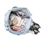 Bolsa de Academia e Viagem Feminina Multifuncional Azul Bebê Urbanno, vista interna com fones de ouvido, câmera, garrafa e roupas, e um par de tênis no compartimento lateral, exibindo sua organização.