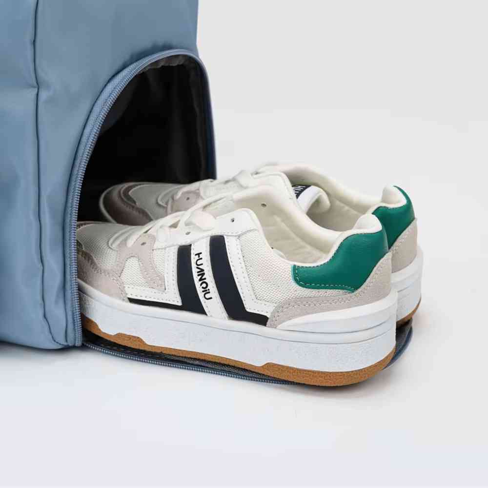 Bolsa de Academia e Viagem Feminina Multifuncional Azul Urbanno, detalhe do compartimento lateral aberto com um par de tênis brancos, verde e preto, evidenciando o espaço dedicado para calçados.