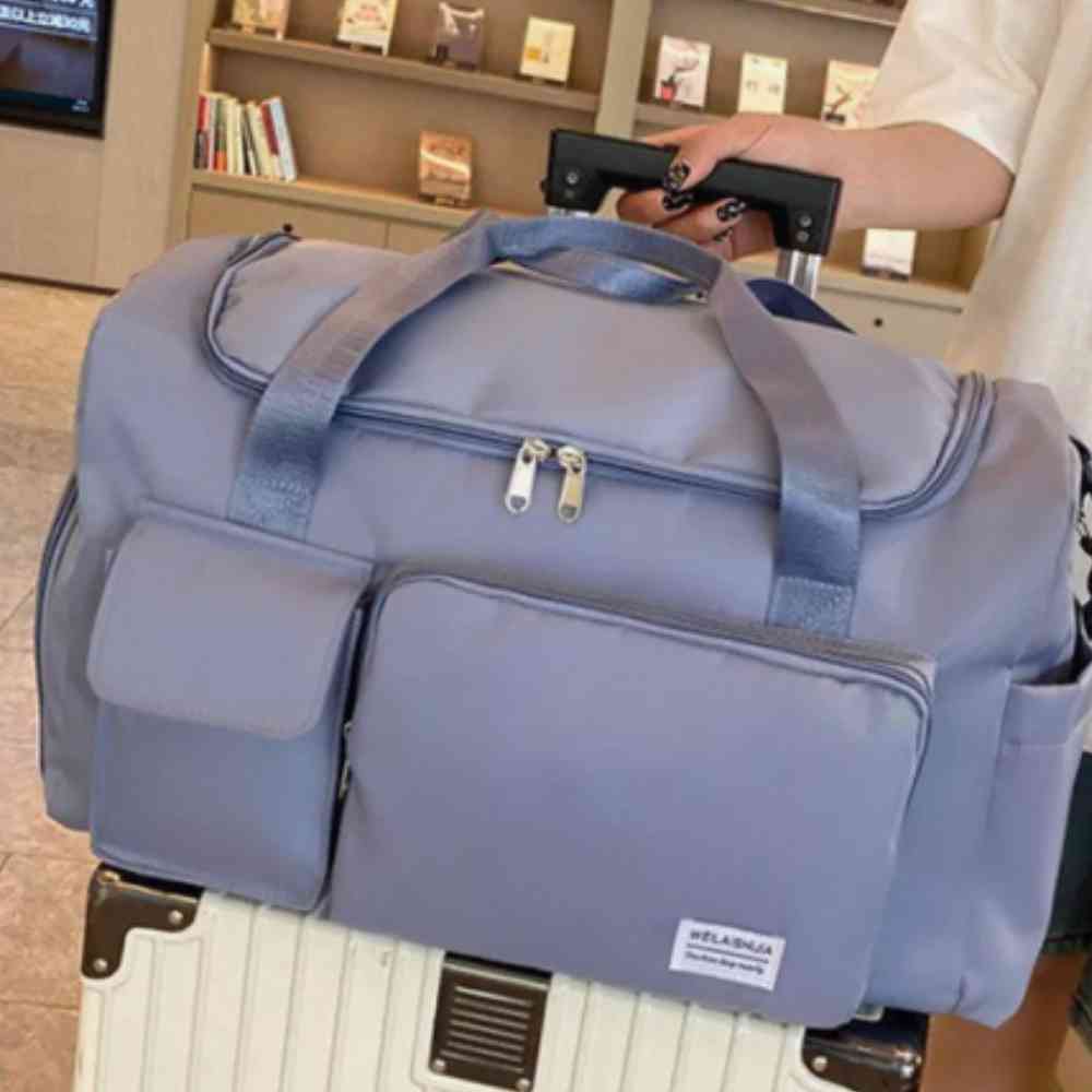 Bolsa de Academia e Viagem Feminina Multifuncional Azul Urbanno, acoplada à alça de uma mala de viagem clara, com foco nos detalhes dos bolsos frontais e zíperes, destacando o uso prático.