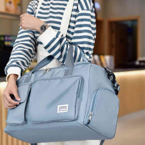 Bolsa de Academia e Viagem Feminina Multifuncional Azul Urbanno, sendo carregada no ombro por uma pessoa com blusa listrada, demonstrando seu tamanho e praticidade para uso diário ou viagens.