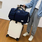 Bolsa de Academia e Viagem Feminina Multifuncional Azul Escuro Urbanno, acoplada à alça de uma mala de viagem clara e sendo transportada por uma pessoa, demonstrando sua praticidade para viagens.
