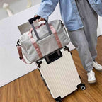 Bolsa de Academia e Viagem Feminina Multifuncional Cinza com Alça Rosa Urbanno, acoplada à alça retrátil de uma mala de viagem clara, sendo transportada por uma pessoa, demonstrando sua praticidade para viagens.