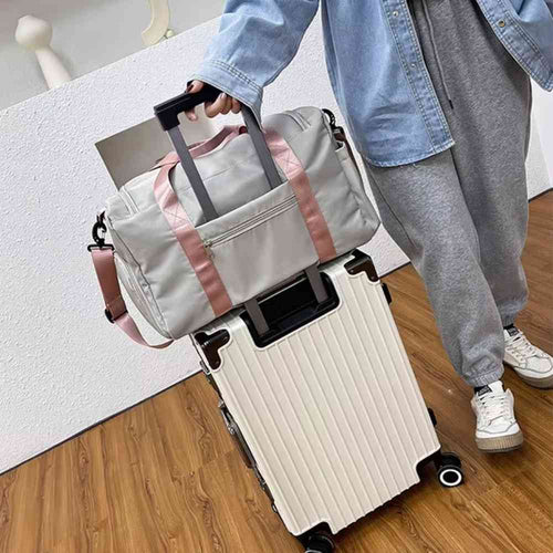 Bolsa de Academia e Viagem Feminina Multifuncional Cinza com Alça Rosa Urbanno, acoplada à alça retrátil de uma mala de viagem clara, sendo transportada por uma pessoa, demonstrando sua praticidade para viagens.