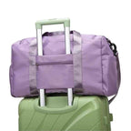 Bolsa de Academia e Viagem Feminina Multifuncional Roxa Urbanno, acoplada à alça retrátil de uma mala de viagem verde, sendo transportada, demonstrando sua praticidade para viagens.