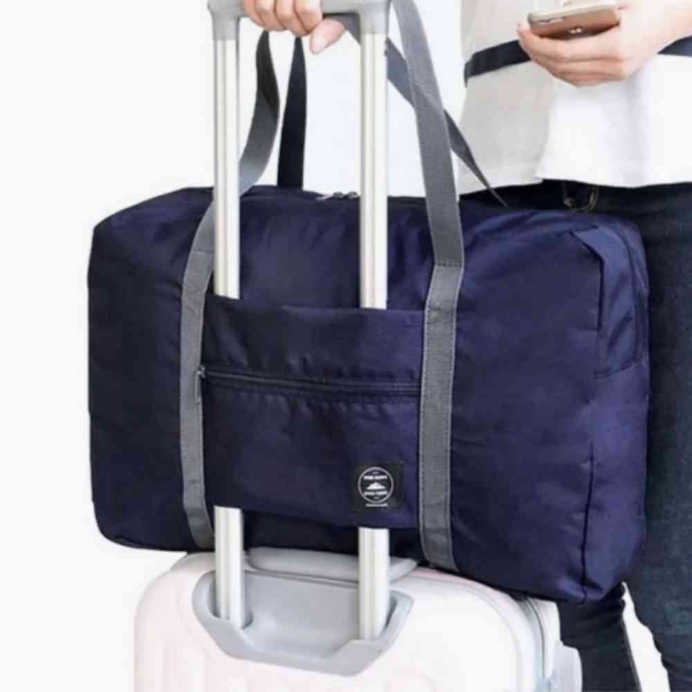 Bolsa de Academia e Viagens Dobrável Azul Escuro Urbanno, acoplada à alça de uma mala de viagem, sendo transportada por uma pessoa, demonstrando sua praticidade para o dia a dia e viagens.