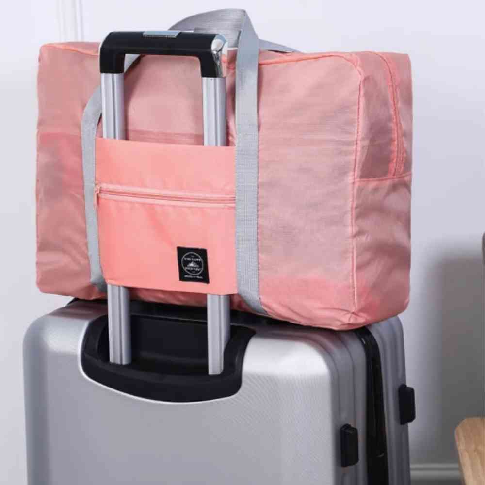 Bolsa de Academia e Viagens Dobrável Rosa Salmão Urbanno, acoplada à alça de uma mala de viagem prateada, com foco no encaixe seguro e prático para transporte.