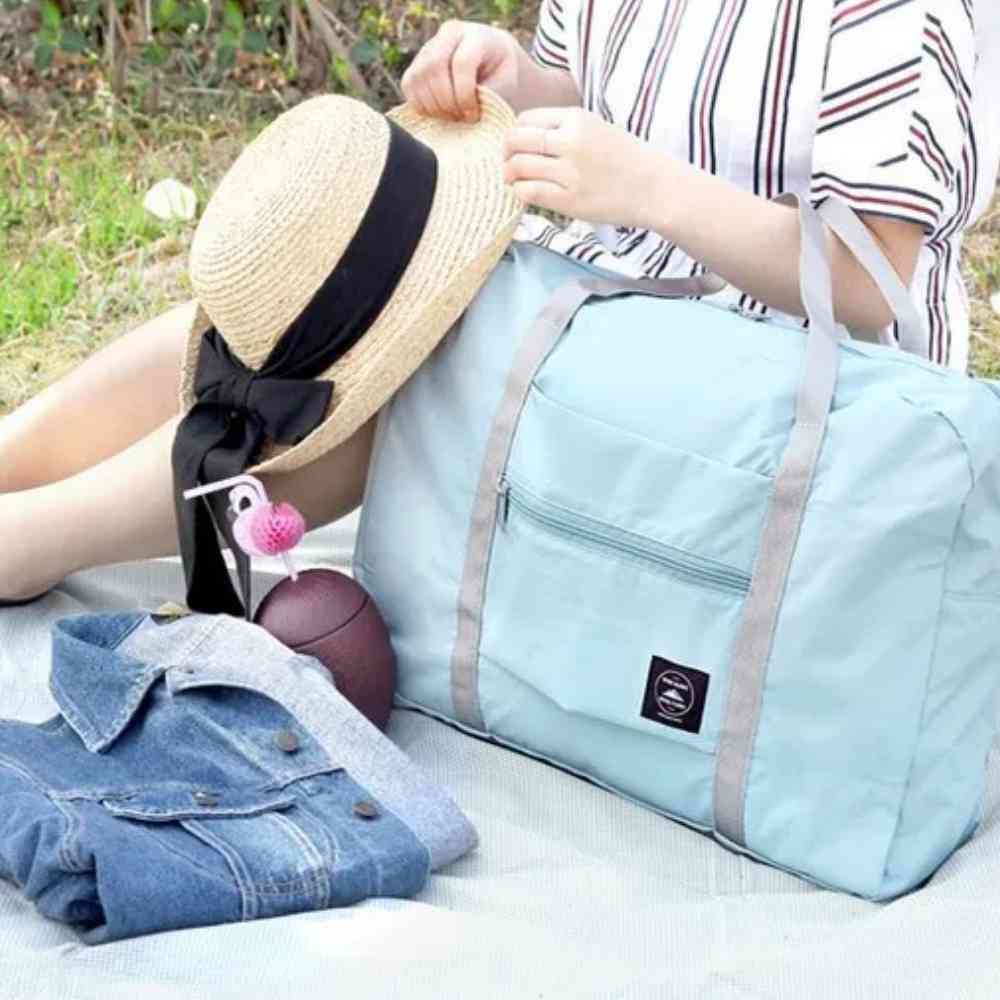 Bolsa de Academia e Viagens Dobrável Verde Água Urbanno, em um cenário de piquenique com chapéu, casaco e outros itens, demonstrando sua versatilidade para diversas atividades ao ar livre.