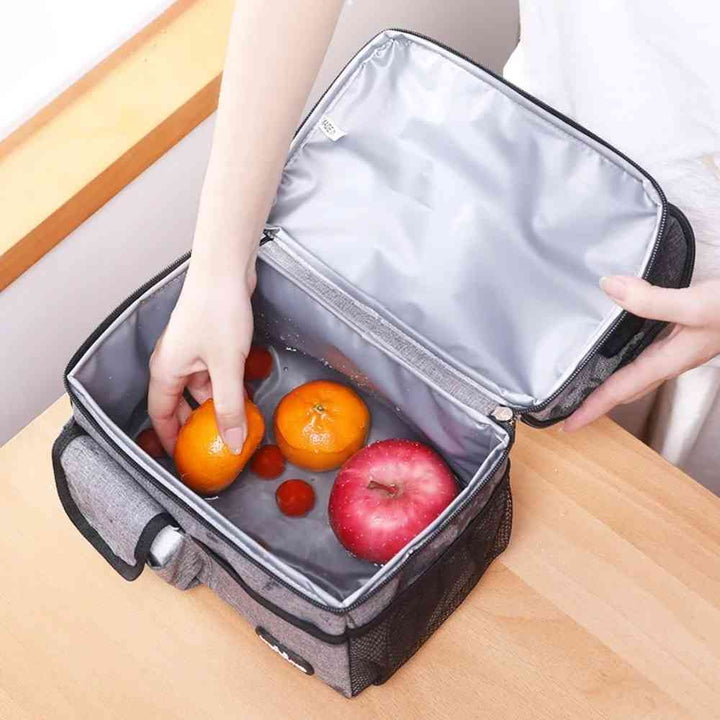 Bolsa Térmica Grande para Marmita com Duplo Compartimento 10L Urbanno cinza, aberta com mãos colocando frutas e tomatinhos no compartimento superior, mostrando o interior impermeável para fácil limpeza urbanno