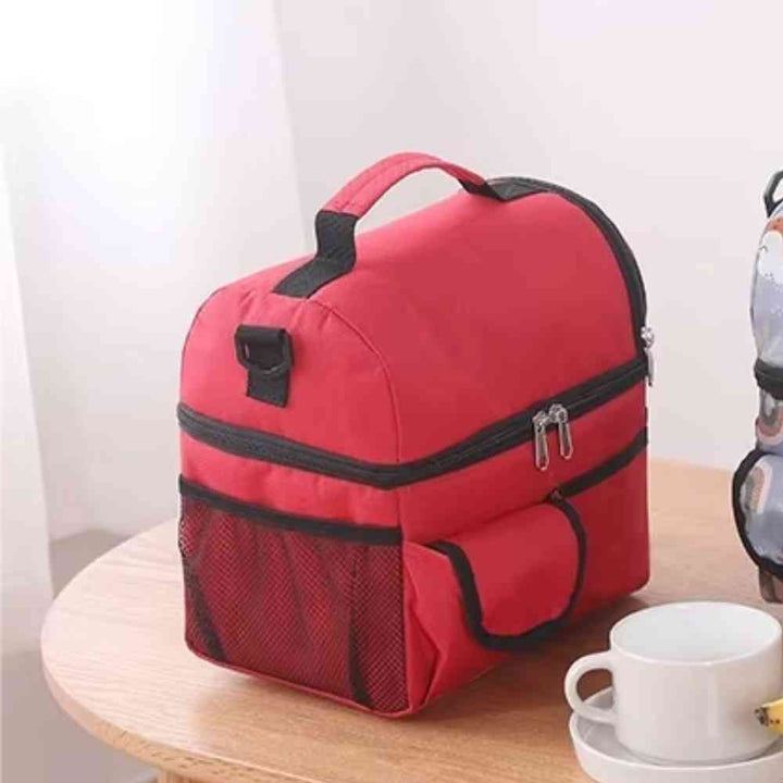 Bolsa Térmica Grande para Marmita com Duplo Compartimento 10L Urbanno vermelha, vista lateral em uma mesa, mostrando bolso de rede, alça de ombro e xícaras ao lado, ideal para refeições em qualquer lugar urbanno