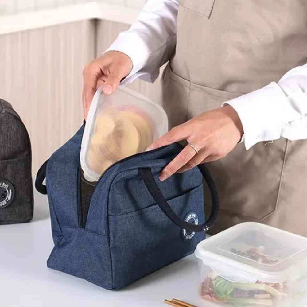 Bolsa Térmica para Marmitas e Dietas Urbanno azul, sendo preenchida com um pote de alimento em ambiente de cozinha