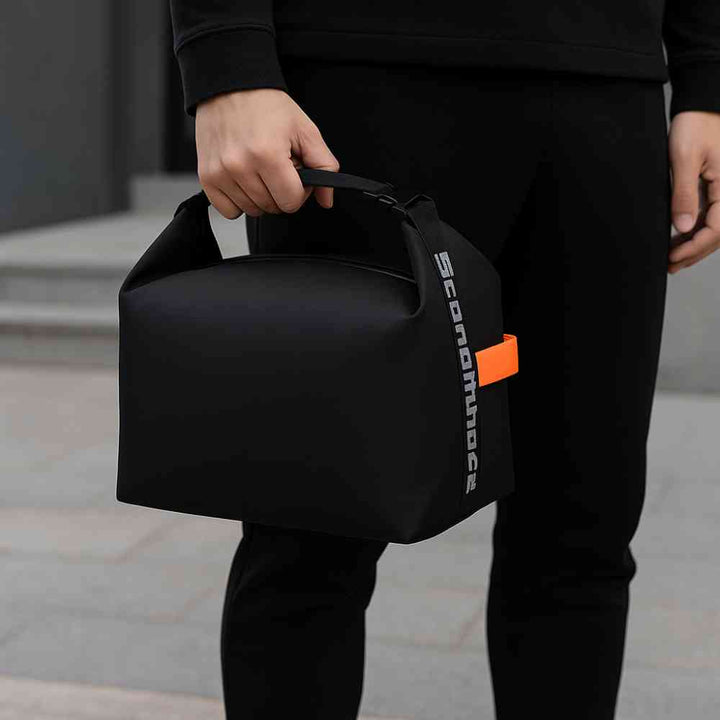Bolsa Térmica Minimalista Urbanno preta, sendo carregada por uma pessoa ao lado do corpo em ambiente externo, destacando portabilidade