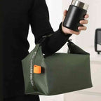 Bolsa Térmica Minimalista Urbanno verde, sendo segurada por uma mão enquanto a outra segura um pote térmico, em ambiente interno