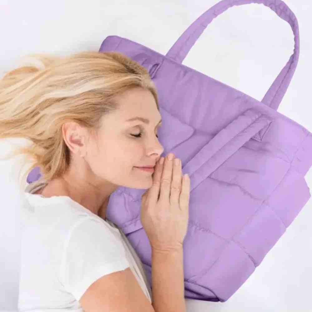 Mulher com cabelo loiro deitada, abraçando a Bolsa Tote de Academia e Dia a Dia Feminina Acolchoada Urbanno lilás, simulando conforto e maciez