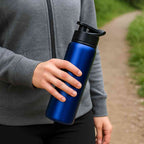 Garrafa de Academia e Hidratação em Alumínio 600ml Urbanno azul, sendo segurada por uma pessoa em uma trilha ao ar livre, demonstrando uso em atividades físicas