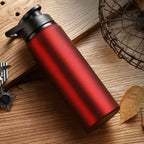 Garrafa de Academia e Hidratação em Alumínio 600ml Urbanno vermelha, sobre superfície de madeira rústica com detalhes de folhas secas e uma cesta ao fundo