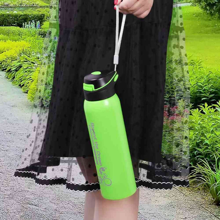 Mulher segurando a Garrafa de Academia Térmica com Canudo e Alça 500ml Urbanno verde pela alça branca, em ambiente externo com folhagem verde ao fundo, demonstrando a portabilidade para atividades ao ar livre urbanno