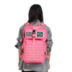 Mochila Feminina Exército Militar Tática 50L Rosa Urbanno, sendo usada nas costas por uma mulher com jaqueta jeans, com patches das bandeiras do Brasil e dos EUA, demonstrando o ajuste e o design.