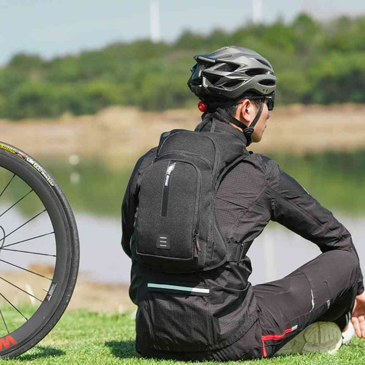 Mochila de Hidratação 10L WEST BIKING com Reservatório 2L Ultraleve Preta Urbanno, sendo usada por um ciclista de costas, sentado na grama com sua bicicleta, demonstrando o ajuste ergonômico e o conforto durante atividades como o ciclismo.