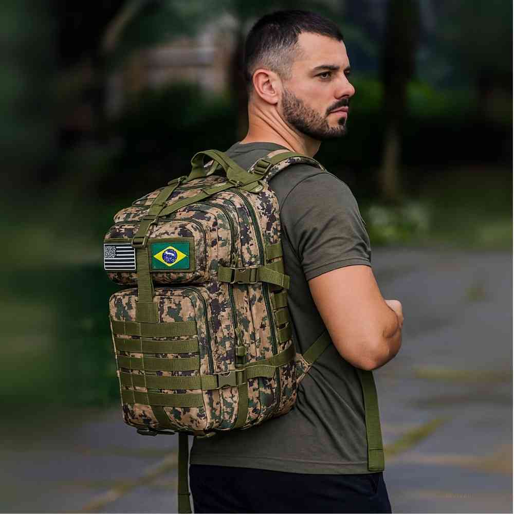 Mochila Militar Tática Impermeável 50L Verde Camuflagem Urbanno, sendo usada nas costas por um homem de camiseta militar, com patches das bandeiras dos EUA e do Brasil, em ambiente externo.