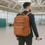 Homem de terno azul usando a Mochila Notebook 15.6" em Couro PU Minimalista USB Marrom Caramelo Urbanno nas costas, puxando uma mala, demonstrando seu uso elegante e prático para viagens de negócios.