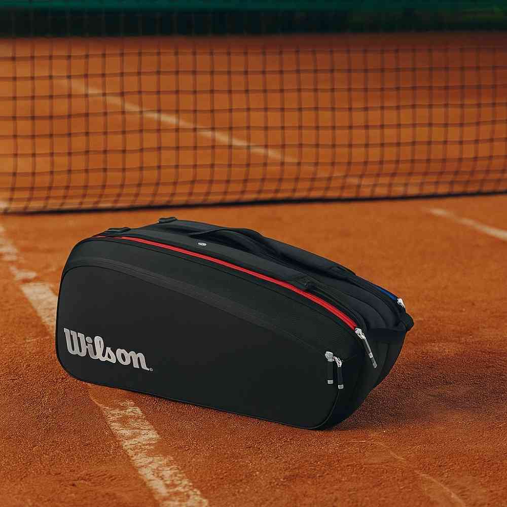 Mochila Raqueteira Wilson Tênis para 9 Raquetes Térmica Preta Urbanno, em uma quadra de saibro, com a rede de tênis ao fundo, pronta para a partida.