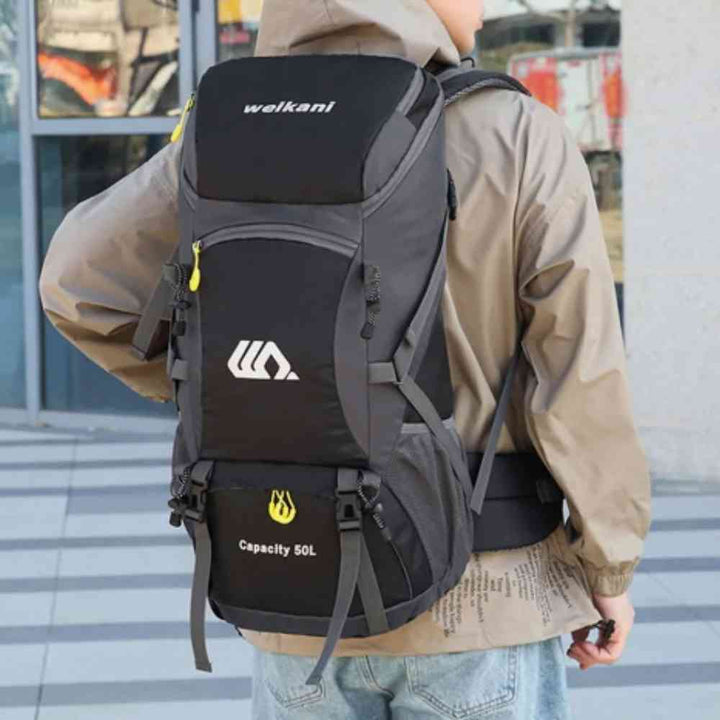 Homem usando a Mochila de Viagem e Camping 50L Aventura Impermeável Urbanno preta nas costas, em ambiente urbano com prédios ao fundo, demonstrando o tamanho e como veste para aventuras urbanno