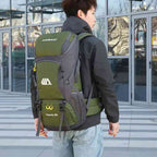 Homem jovem usando a Mochila de Viagem e Camping 50L Aventura Impermeável Urbanno verde oliva nas costas, em ambiente urbano com prédios de vidro ao fundo, demonstrando o tamanho e como veste para aventuras urbanno