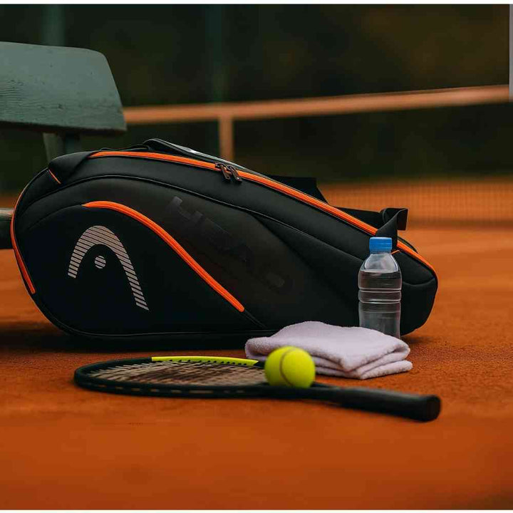 Raqueteira Head Hard Shell para 6 a 9 Raquetes de Tênis Preta e Laranja Urbanno em quadra de saibro, com raquete, bola, toalha e garrafa d'água ao lado, pronta para o jogo.